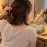 乾いた部屋の鏡の前で、髪を持ち上げて後頭部と内側を確認する女性。