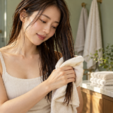 肩へ分けた濡れ髪を、折ったタオルで包んで押さえる女性。